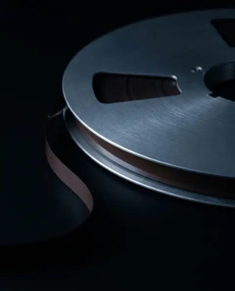 A reel of magnetic recording tape in darkness, its loose end curling into shadow.