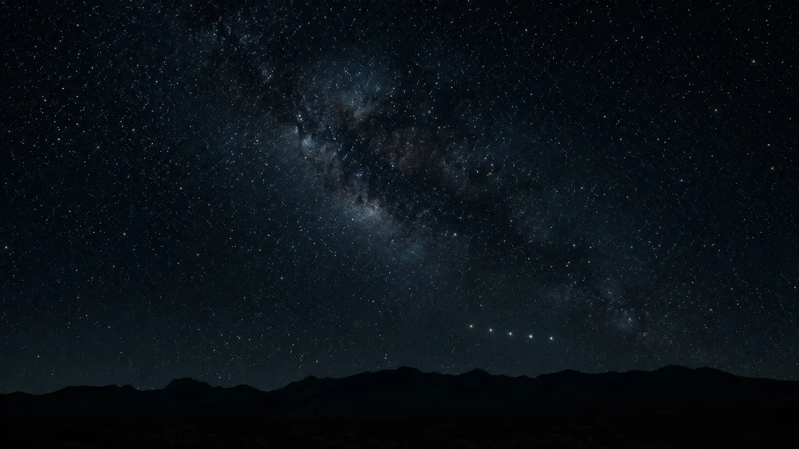 Five evenly spaced points of light hanging above a dark desert ridge under the Milky Way.